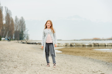 Adorable little girl of 8-9 years old playing by the lake, wearing grey trousers and long cardigan