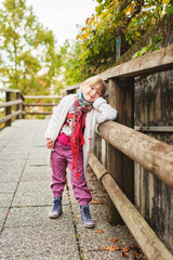 Outdoor portrait of a cute little girl wearing red trousers, colorful boots and white knitted jacket