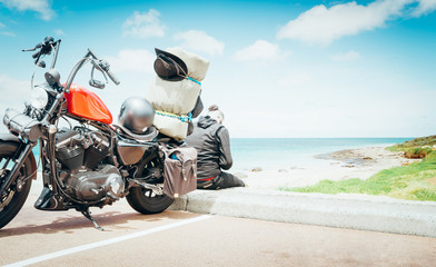 Biker man wearing a leather jacket and sunglasses sitting on his vintage motorcycle back with a...