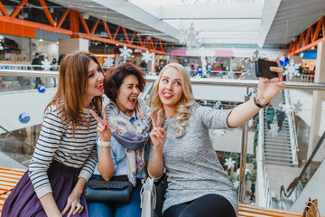 Group of cute girl friends doing some shopping at a mall and taking a selfie with a smartphone