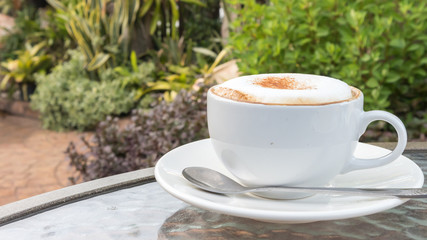 Closeup A cup of hot cappuccino on glass table with garden natur
