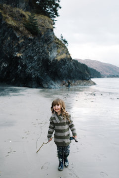Girl walking on beach, holding stick