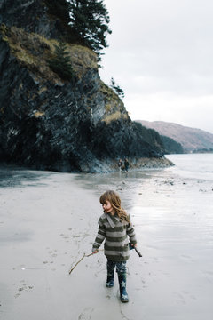 Girl walking on beach, holding stick