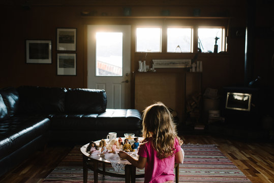 Young girl playing with dolls in living room, rear view
