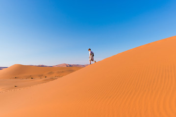 Fototapeta na wymiar Tourist walking on the scenic dunes of Sossusvlei, Namib desert, Namib Naukluft National Park, Namibia. Afternoon light. Adventure and exploration in Africa.