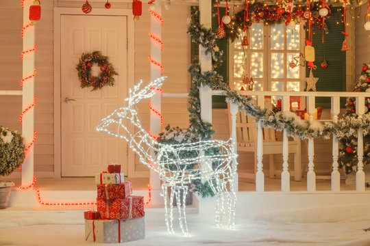 Vintage Christmas decorated house with illuminated deer in front of the door, gift boxes, 