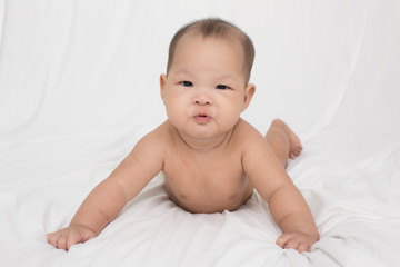 smiling surprised baby lying on a white bed.  Baby born in Thailand, Asia.  Infants aged 5 months