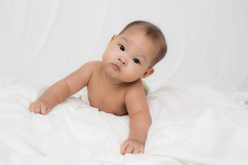 Smiling surprised baby lying on a white bed. 