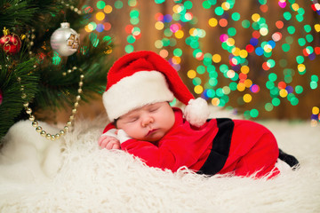 Obraz na płótnie Canvas Portrait of newborn baby in Santa clothes lying under Christmas tree.