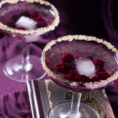 Two alcohol cocktails with berries on purple. Square