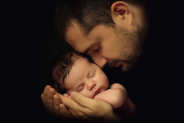 Little 15 days old baby lying securely on his Dad's arms, against a black background