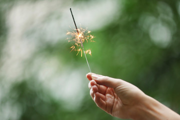 Female hand holding sparkler on blurred background