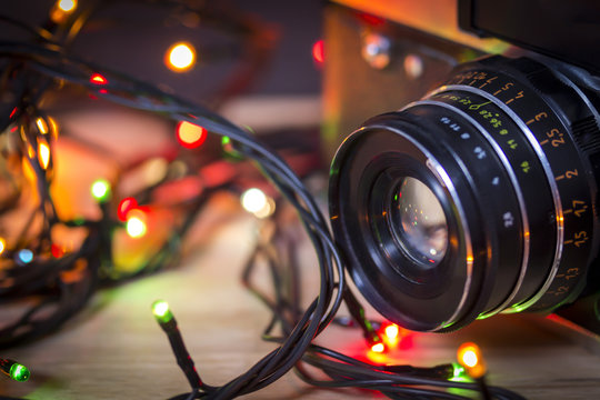 Vintage camera lens with garland christmas lights on colorful bokeh background. Mockup for holiday new year greeting card