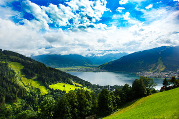 Fototapeta na wymiar View over Zeller See lake. Zell Am See, Austria, Europe. Beautiful green meadows and pines at foreground, Alps at background.