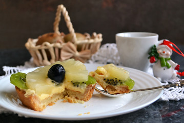 Festive breakfast. Fresh fruit tart on white porcelain plate with silver spoon, petite cup of coffee, christmas decoration.