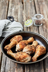 Hot Meat Dishes. Fried chicken legs with pepper in a frying pan on a wooden surface.