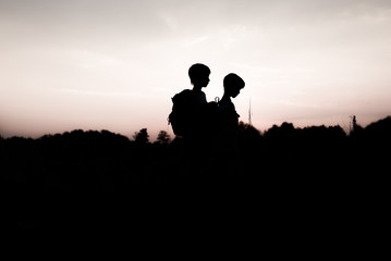 Fototapeta na wymiar Silhouettes of kids hiking at sunset. Happy boy and girl on summer vacation in mountains. Tourists walking on hill edge carrying backpacks. Summertime. Little children traveling. Friendship concept.