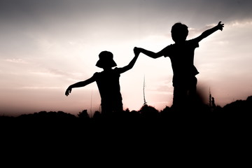 Silhouettes of children jumping off a cliff at sunset. Boy and girl jump high holding hands....