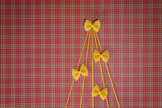 Christmas tree silhouette made of spaghetti and bow tie pasta on red squared background. Flat lay. Top view. Winter holidays concept