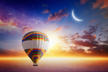 Hot air balloon rises very high in sunset sky above glowing clou