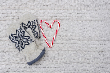 Pair of mittens and candy canes heart on white knitted background