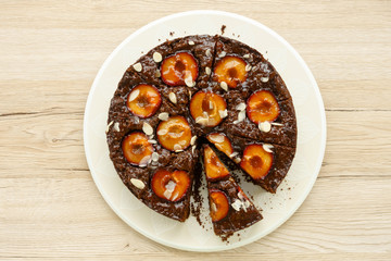 Whole  Homemade Sticky Chocolate Plum Cake isolated on light brown wooden background.