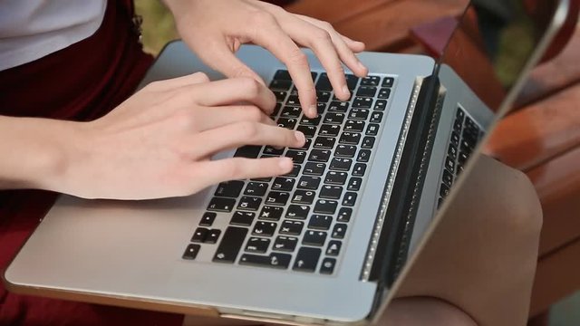 Closeup of girl's hands on the laptop. Girl typing, using laptop outdoors.