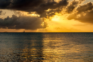 Distant sail boat on golden tropical island sunset