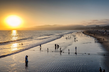 Serene California beach sunset with silhouettes of people on wet sand