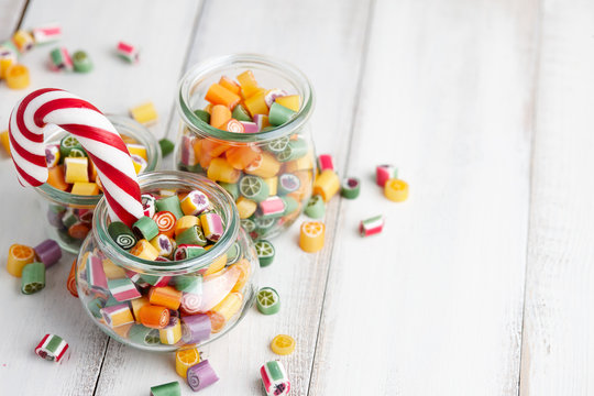 Colorful lollipops and candy canes in glass jars on white wooden background
