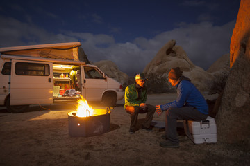 Two friends sitting by a fire near their camper van in Joshua Tree National Park.  California