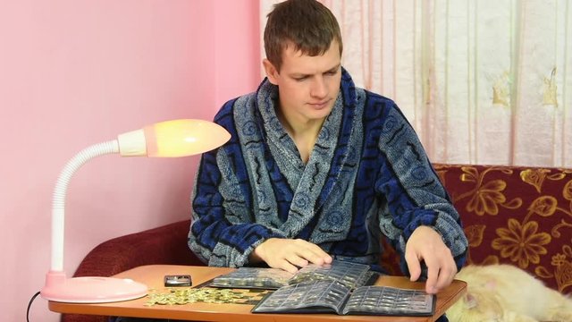 A young man in a dressing gown watching his collection of coins in albums