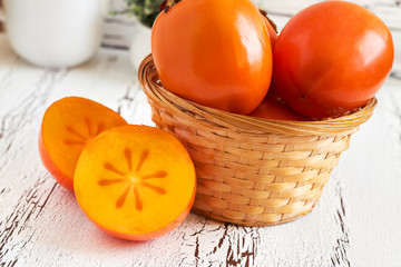 Japanese persimmon (Diospyros kaki) in woven basket on white rustic wooden background