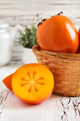 Japanese persimmon (Diospyros kaki) in woven basket on white rustic wooden background. Copy space