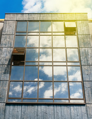 Sunny flare over abstract glass-concrete facade of a modern building covered in reflective plate glass with clouds refletetions