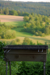 Empty portable BBQ grill in front of a fresh green summer landscape