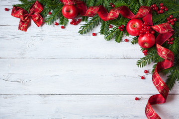 Christmas wooden background with branches of trees, apples, berries and red ribbon