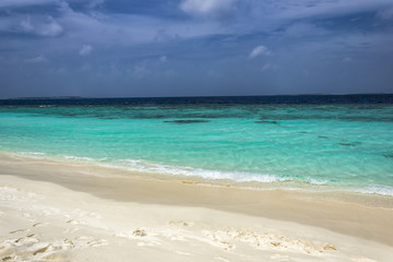 Fototapeta na wymiar Typically Maldivian Landscape shot on a cloudy day with turquoise ocean, blue sky and white sandy beach. An amazing color combination of three tones of blue.