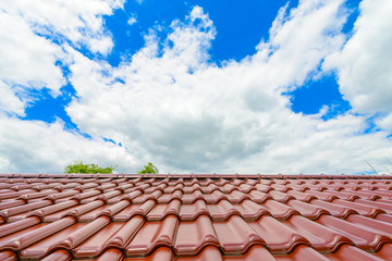 Obraz premium Brand new red rooftop roof tiles against blue sky and clouds