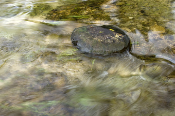 Firm as a rock, stone with water moving around it. Water is blurred because of streaming and...