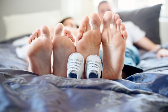 Feet of expectant parents and tiny shoes.