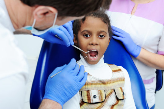 portrait of an African baby girl with black skin in the dental chair. The dentist examines the mouth and teeth of a young child