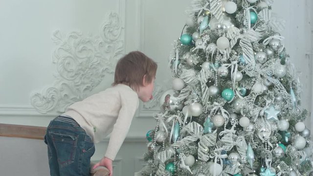 Little boy sticking his tongue out at his own reflection in the bauble on the Christmas tree