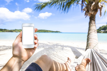 Using smartphone on a tropical paradise beach sitting in hammock