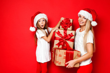 Happy mother and daughter in Christmas caps with gift wrapped in craft paper and red ribbons on red background. Christmas. Happy family. 