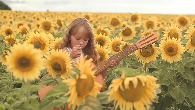 summer outdoor recreation, little girl playing guitar on background of field with sunflowers