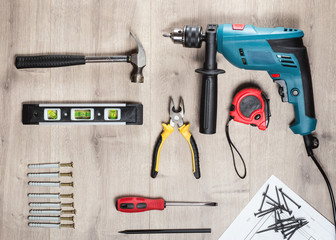 Flat lay Set of construction tools to repair on a wooden surface: drill, hammer, pliers, self-tapping screws, roulette,  level, drawing,  pencil. Top view.