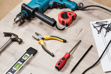 Set of construction tools to repair on a wooden surface: drill, hammer, pliers, self-tapping screws, roulette,  level, drawing,  pencil. Side view.