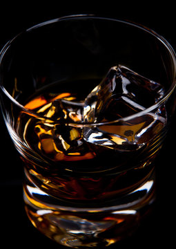 Glass of whiskey with golden ice cubes on black