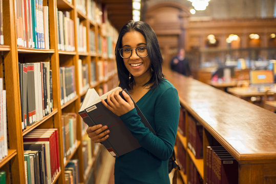 Happy smiling african american student girl reading book at library wearing eyeglasses. Woman studying in the library. People learning getting college degree concept..